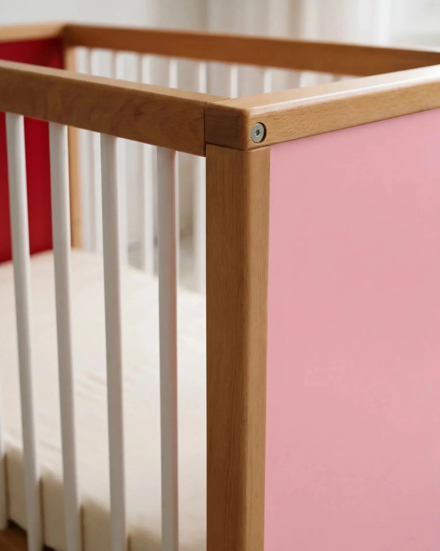Close-up corner detail of the interchangeable panel on the Pink and Red Bold Baby Cot