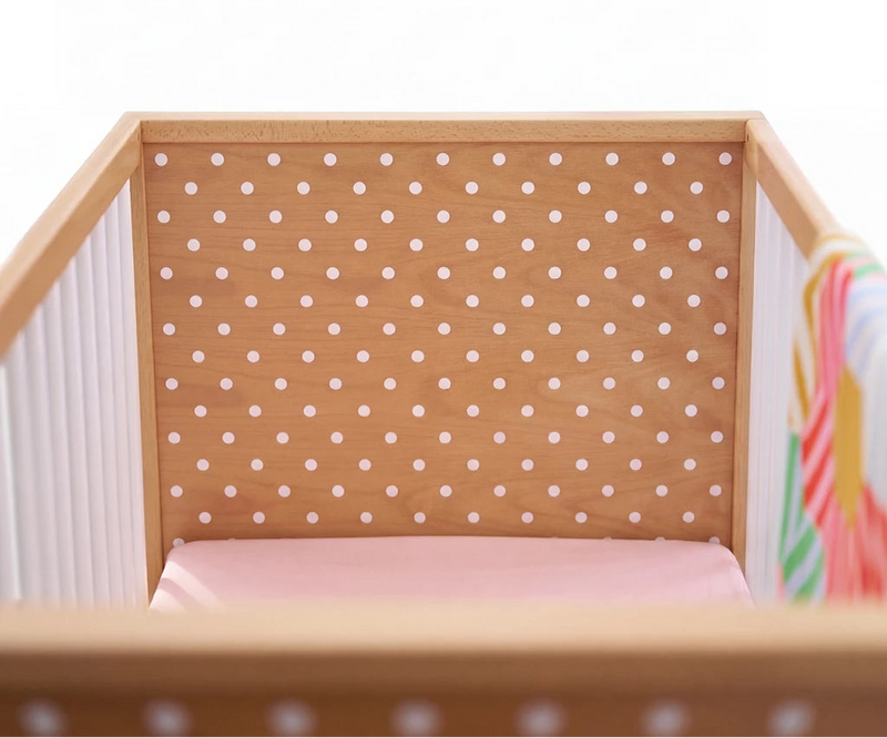 Small wooden crib with a white mattress and polka dot headboard on a white background