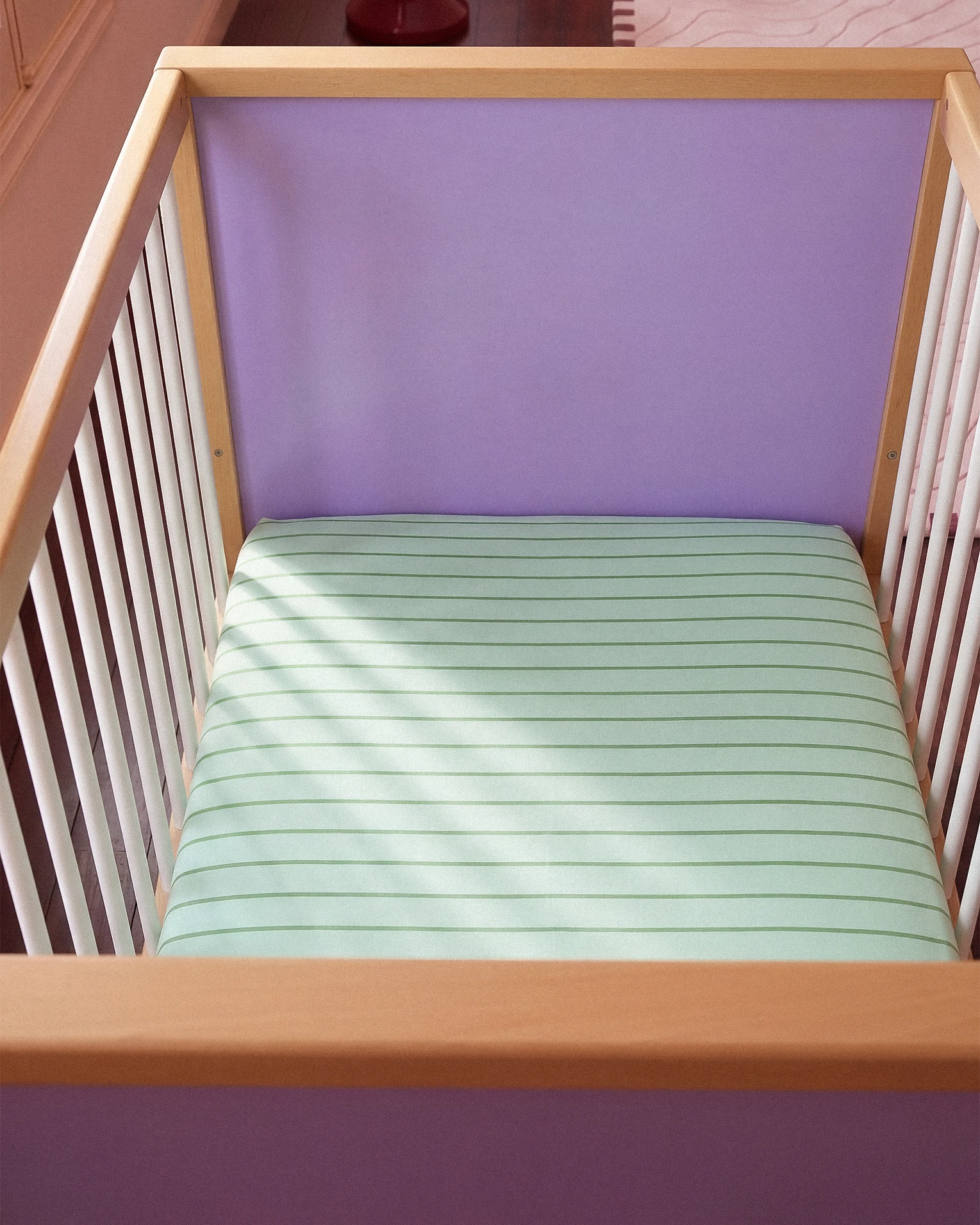 Wooden crib with a mint and green mattress and purple headboard