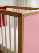 Close-up corner detail of the interchangeable panel on the Pink and Red Bold Baby Cot