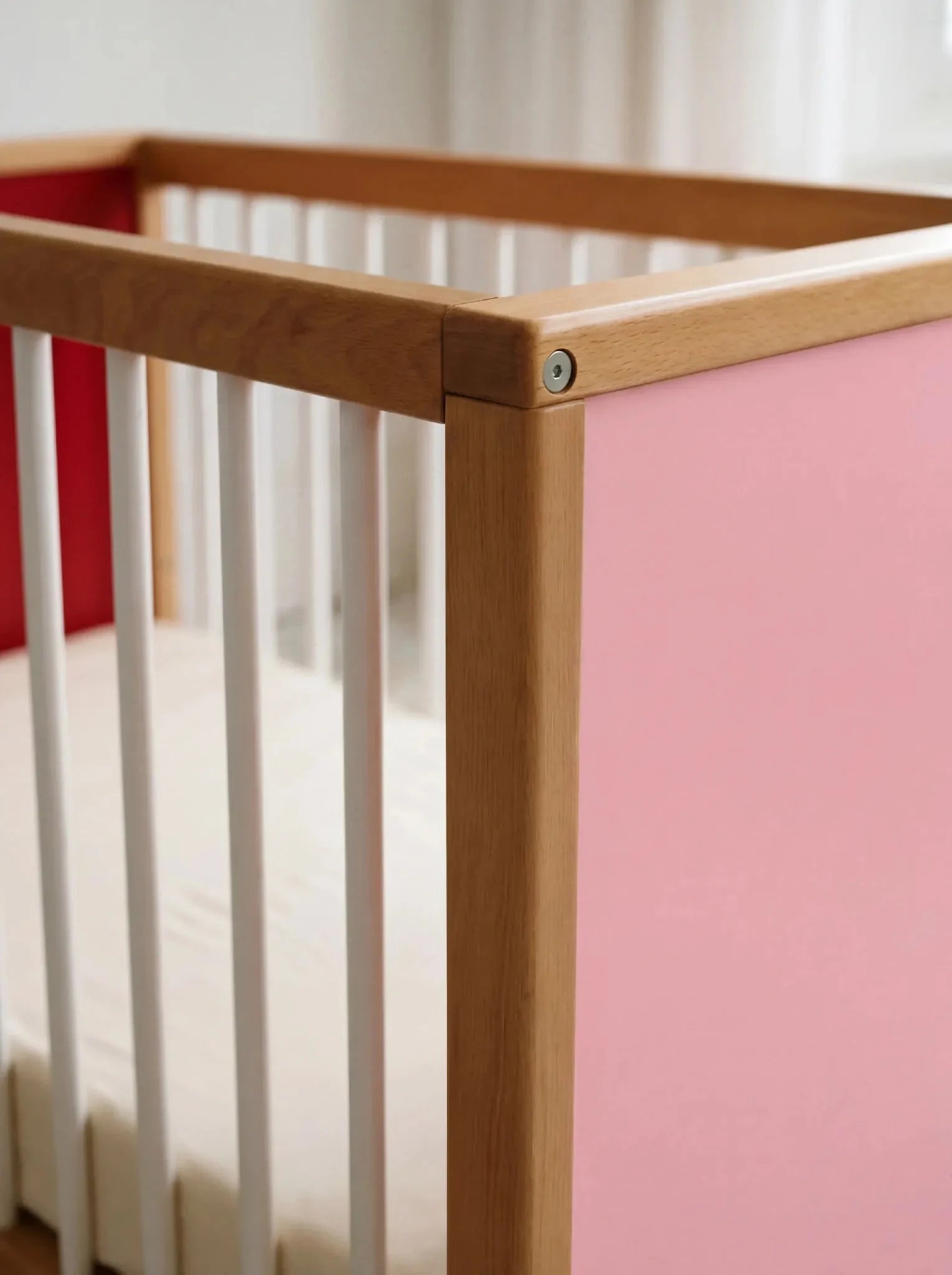 Close-up corner detail of the interchangeable panel on the Pink and Red Bold Baby Cot