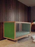 Green and Mint Bold Baby Cot positioned against a timber wall in a stylish nursery.
