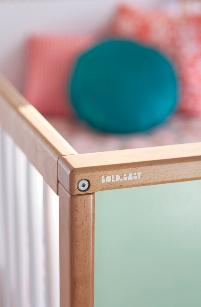 Bold Baby logo on corner of cot with red and green cushions in the background