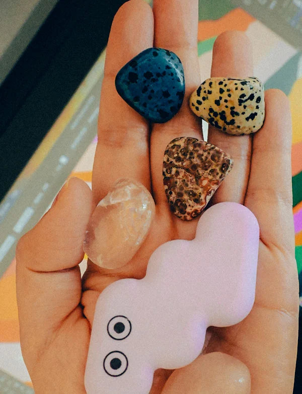 Hand holding four different colored stones with a colorful background