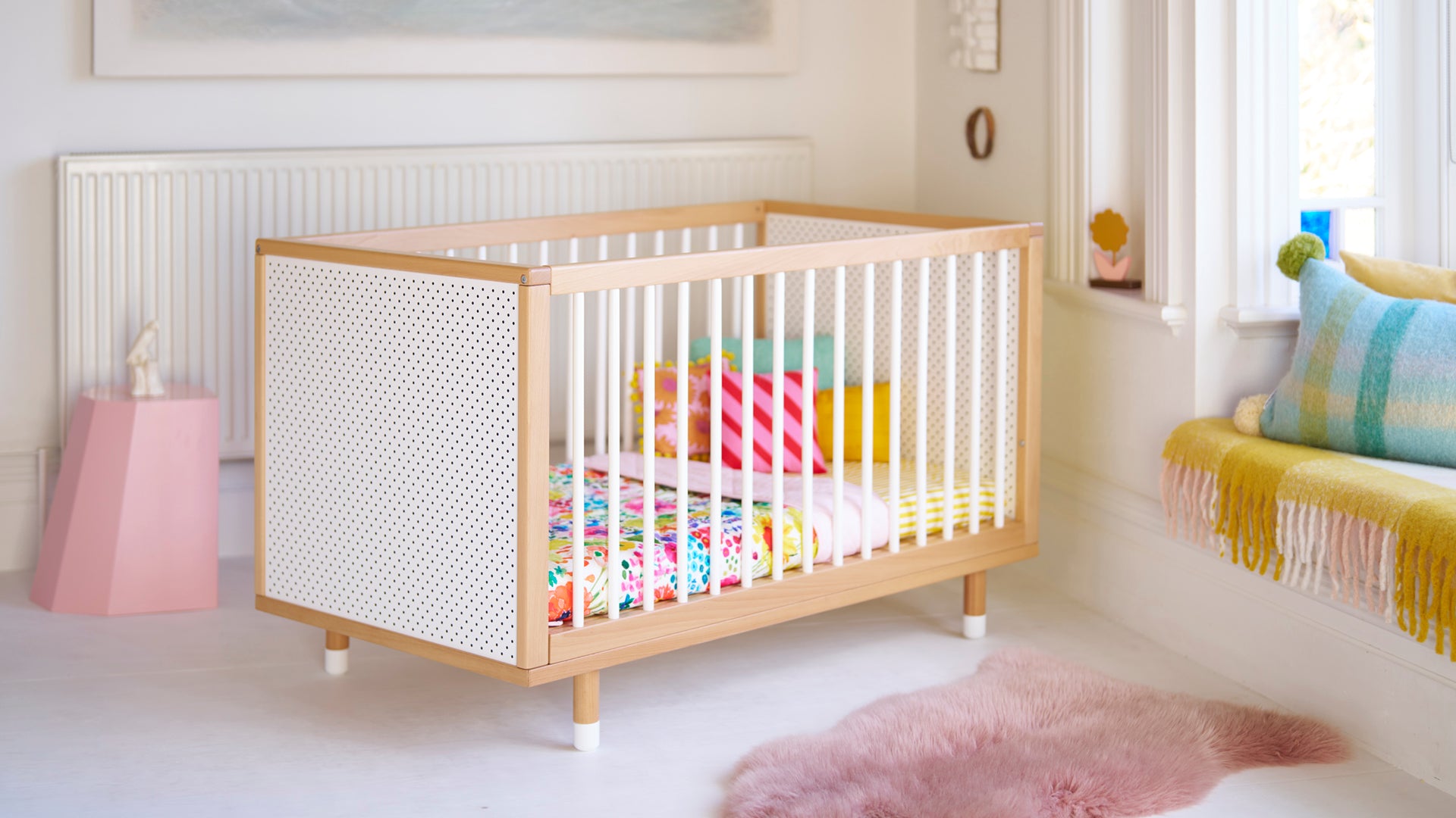A three quarter view of a cot with a colourful blanket