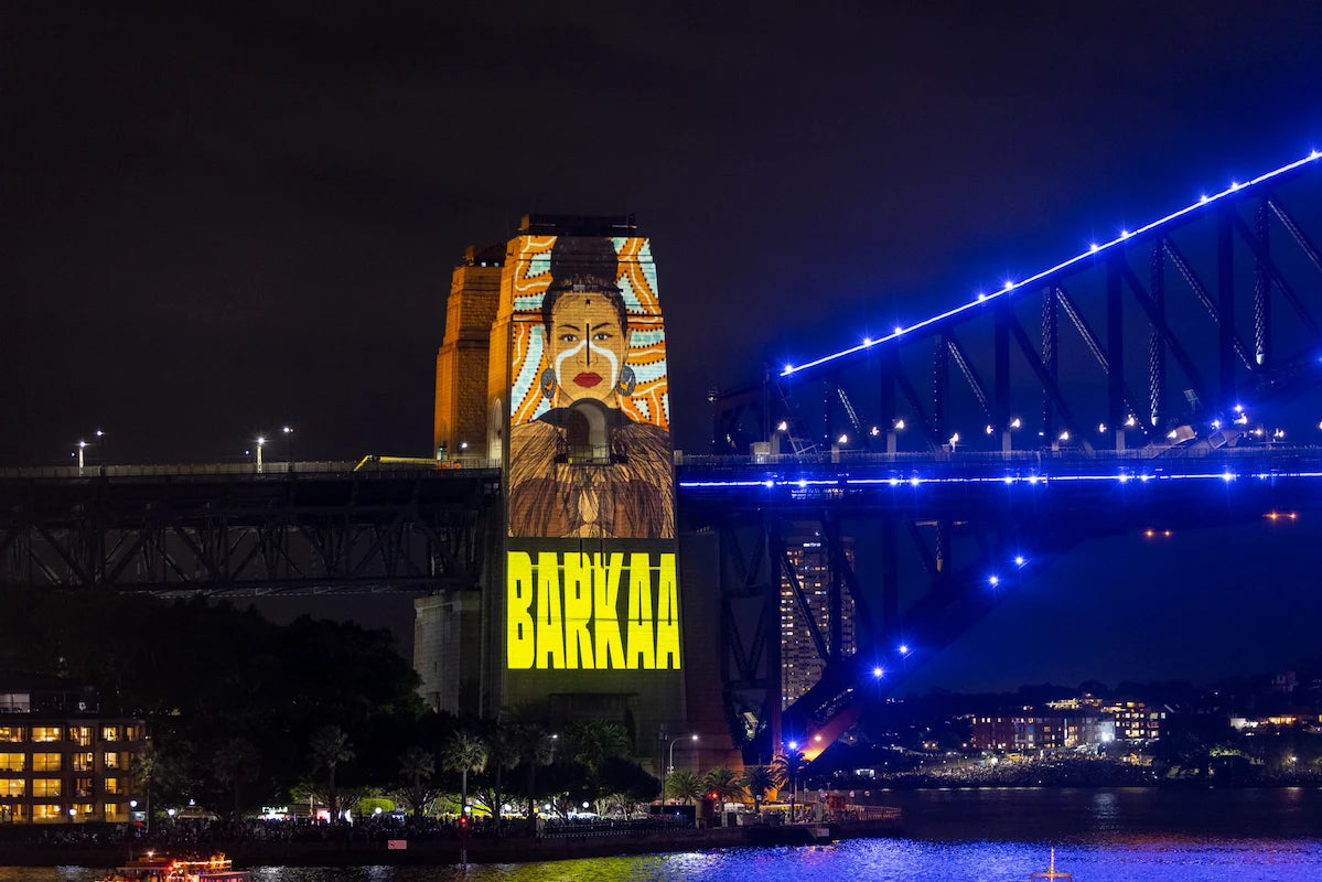 Artwork being projected on to a tower at Sydney harbour bridge at night. The bridge is illuminated with blue lights.