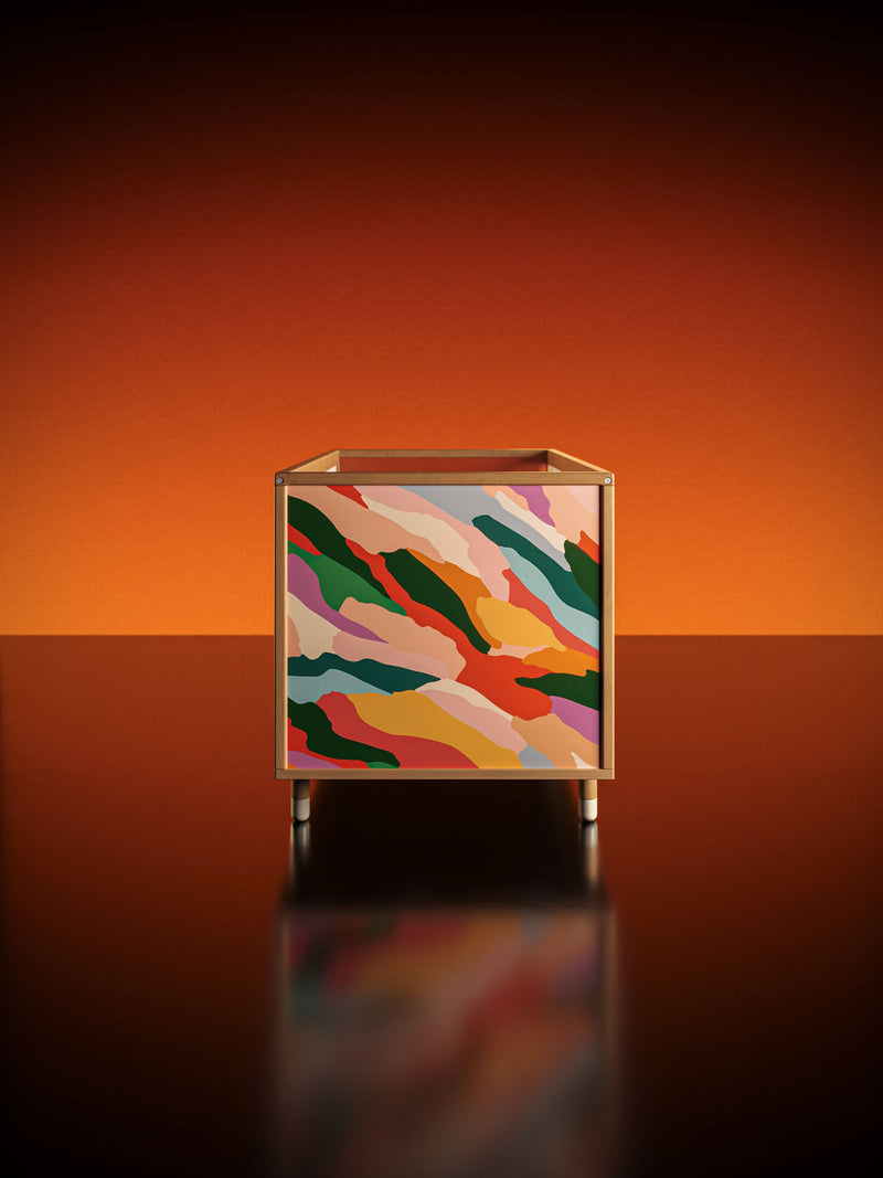 Colourful artwork on a modern cot displayed on a reflective surface with an orange gradient background