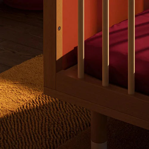 Wooden crib with a maroon mattress on a tufted rug in a stylish nursery