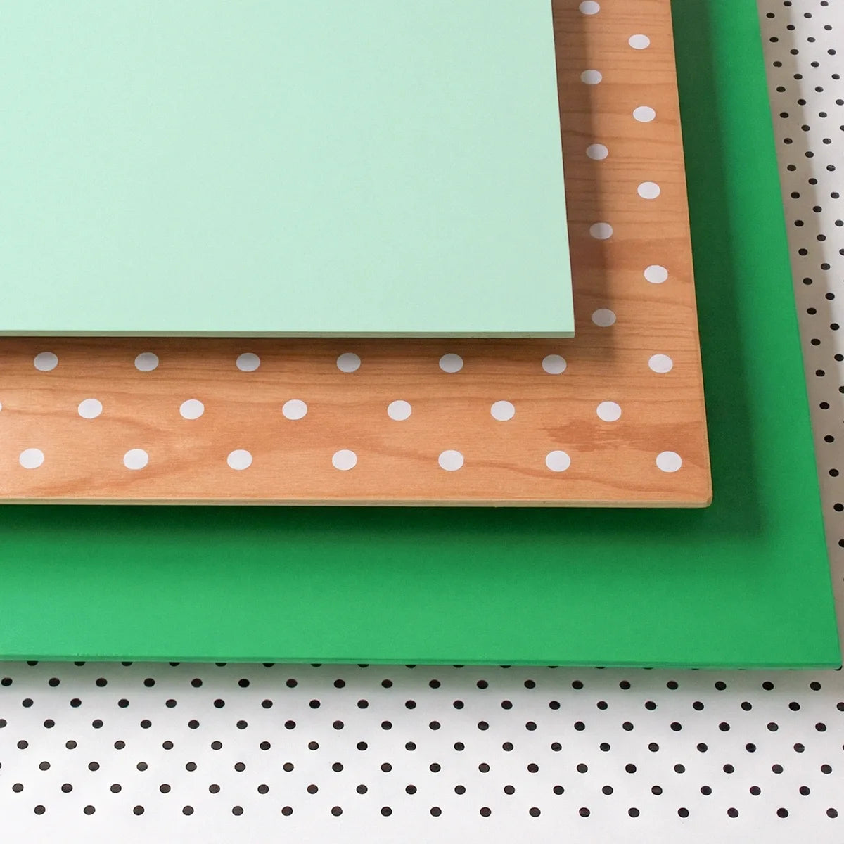 Green paper, wooden board with white polka dots, and green fabric on a pegboard background