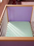 Wooden crib with a mint and green mattress and purple headboard