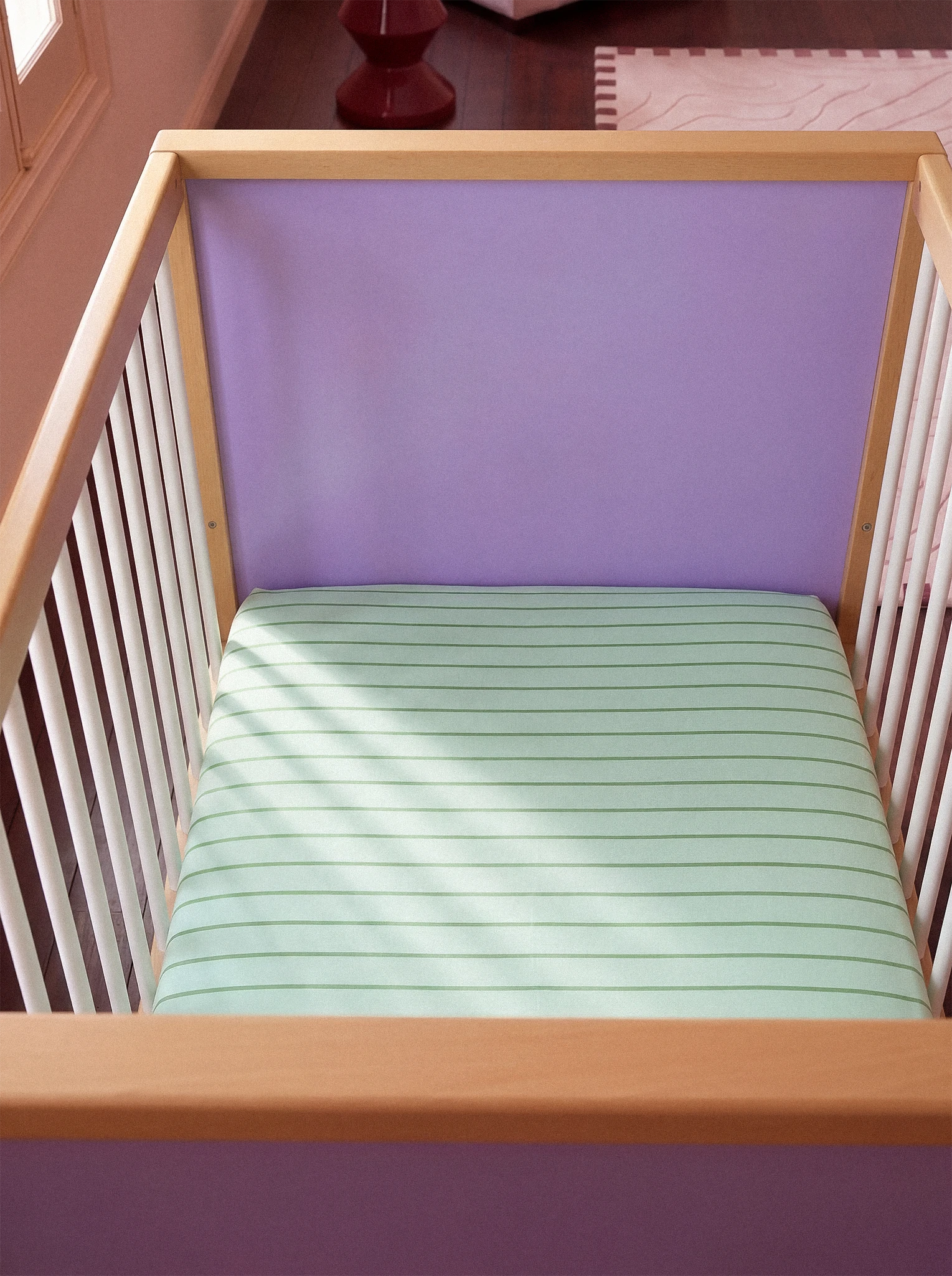 Wooden crib with a mint and green mattress and purple headboard