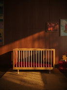 Side view of the Bold Baby Art Series cot by Janelle Burger, with maroon mattress.